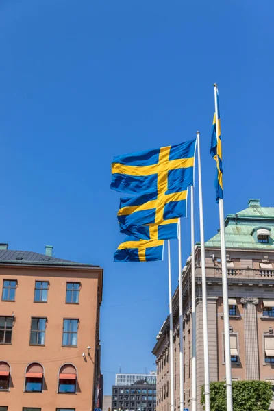 Muitas bandeiras da Suécia em uma barra de metal no ar contra o fundo de um edifício em um dia ensolarado — Fotografia de Stock