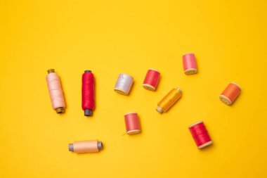 Sarı arka planda çok renkli iplik makaraları ya da dikiş aksesuarları.