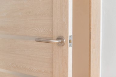 Bir otel veya apartman dairesinde kilitli ve metal saplı parlak ahşap bir kapı aç.