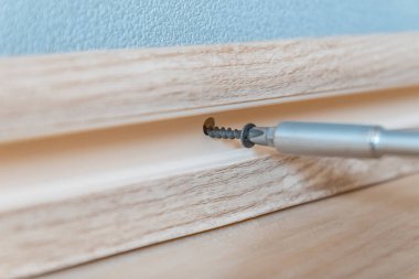 Bir tornavida, vidayı hafif plastik bir süpürgeliğe ve duvara sıkıştırır. Evdeki onarımlar..