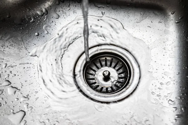 Acqua che scorre lungo il foro nel lavandino in acciaio inox — Foto Stock