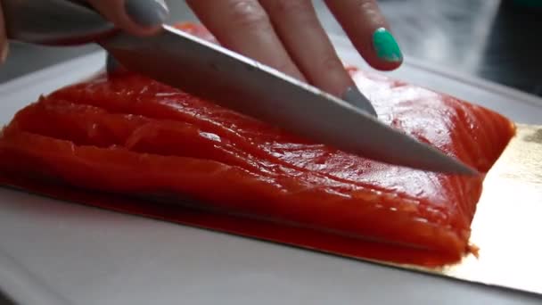 Femmina mano taglia un metallo con un coltello un pezzo di salmone fresco su una tavola di plastica in cucina — Video Stock