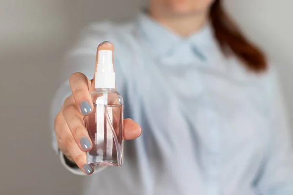 La mano de la mujer sostiene una botella de plástico con líquido desinfectante en aerosol de alcohol sobre un fondo gris — Foto de Stock