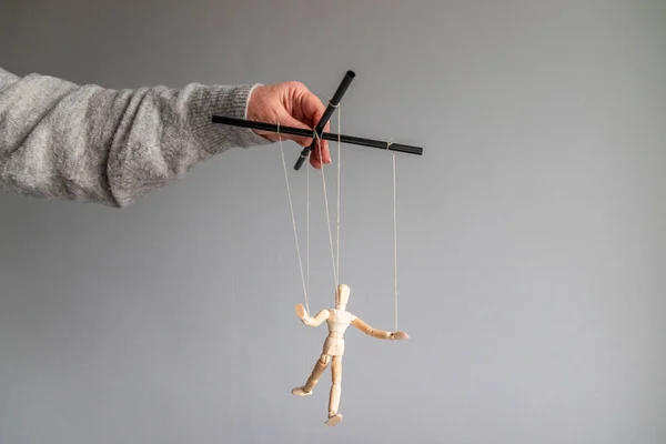 The human hand holds a wooden doll on the clothesline on a gray background with place for text. Power metaphor concept — Stock Photo, Image