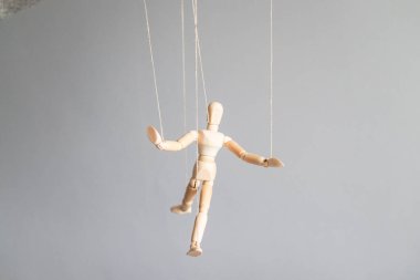 İnsan eli, gri arka planda çamaşır ipinde tahta bir bebek tutuyor. Güç metaforu kavramı