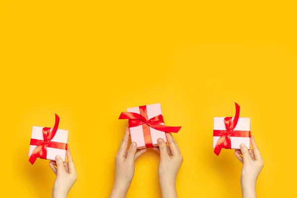 Human hands holds surprise boxes with red bow on a yellow background, top view, flat lay
