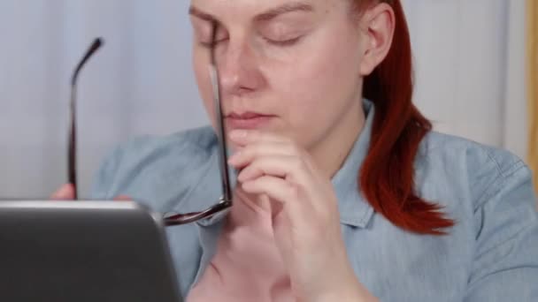 Beautiful young woman removes glasses from her face from fatigue. Remote work on a laptop sitting in the living room. Freelance, quarantine — Stock Video