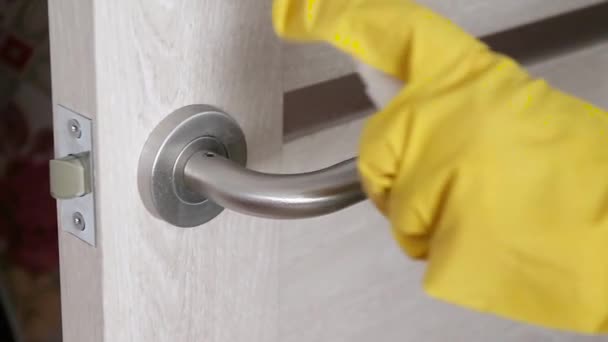 Woman in yellow latex rubber gloves sprays and wipes a doorknob from germs, viruses and bacrea in a home, office or hospital. Coronavirus, Covid 19 — Stock Video