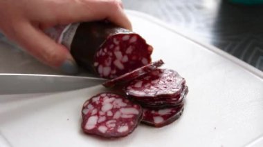 İnsan elleri mutfaktaki kesme tahtasına sosisli salam koyar..