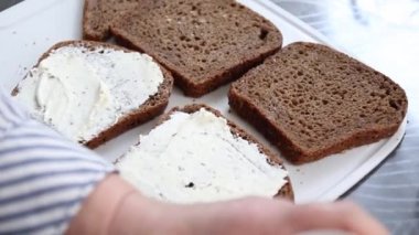 Çok tahıllı ekmeğin üzerinde krem peynirle bıçaklı kadın elleri..