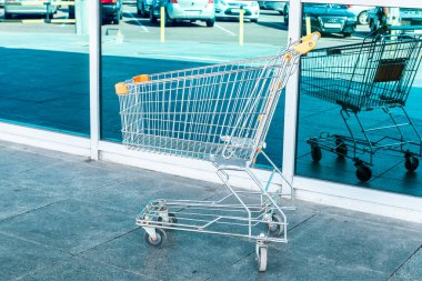 Alışveriş ve mağaza konsepti. Metal bir market arabası cam bir binanın yanında duruyor.