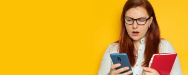 Sarı arka planda baş ağrısı olan gözlüklü genç bir işçi kız. Kadın elinde akıllı telefon ve defterle sorununa bir çözüm bulmaya çalışıyor. Stres, yorgunluk insanlar konsepti.