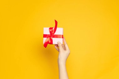 Kadın eli sürpriz bir kutu tutuyor, hediye paketi, Kraft kağıdına sarılı ve kırmızı kurdele sarı arka planda, üst tarafta, düz yerde.