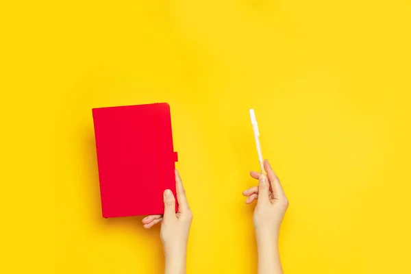 Czerwony pusty notatnik i biały marker w rękach kobiet na żółtym tle z przestrzenią do kopiowania — Zdjęcie stockowe