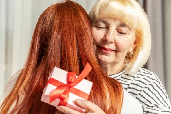 Mujer adulta mamá y su hija abrazándose. Dar un regalo de cumpleaños o de día de las madres —  Fotos de Stock