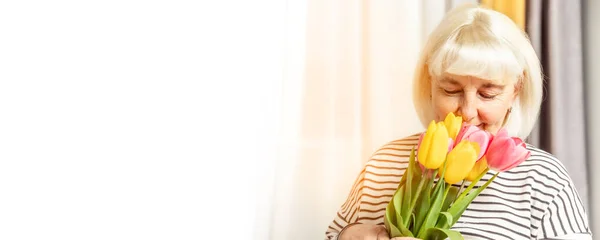 Día Internacional de la Mujer. Mujer rubia adulta huele un ramo de tulipanes copyspace sobre un fondo gris . —  Fotos de Stock