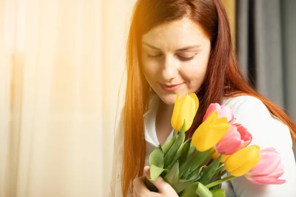 Vrouwendag 8 maart. Mooi meisje in een blauwe katoenen blouse met frisse tulpen boeket in haar handen, ruikt ze op een grijze muur achtergrond — Stockfoto