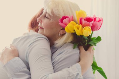 Anneler Günü konsepti. Anne ve küçük kızı sarılıyorlar. Anneler Günün kutlu olsun. Kızı annesini tebrik eder ve bir buket lale çiçeği verir.