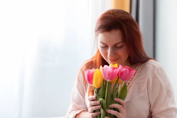 Güzel, uzun saçlı bir kızın portresi elinde bir buket taze lale çiçeği tutuyor ve onları odada kokluyor. Sevgililer Günü, doğum günü konsepti — Stok fotoğraf