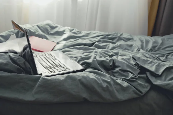Ordenador portátil, libro y teléfono inteligente en una cama gris. Independiente, trabaja en casa, quédate en casa. Formación en línea —  Fotos de Stock