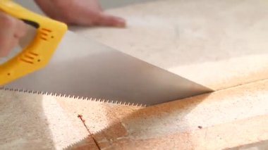 İnsan eli, bir evin güneş ışığıyla testereyle tahta bir tahtayı testereyle keser.
