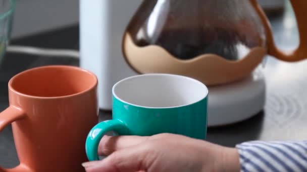 Eine weibliche Hand nimmt zwei farbige Keramiktassen mit einem heißen Kaffeegetränk vom Tisch. — Stockvideo