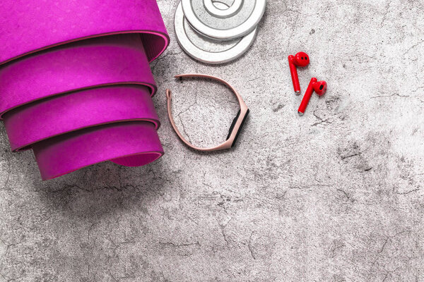 Фиолетовый коврик для йоги, наушники, гантели вес, фитнес-трекер для тренировки на сером фоне с копировальным пространством
