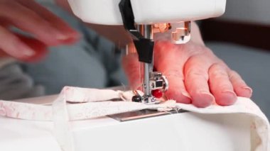 Dikiş işleminin görüntüsünü kapat. Koronavirüs salgını sırasında koruyucu solunum maskeleri dikmek için dikiş makinesi kullanan kadın eller..