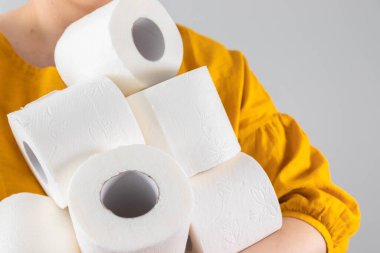 Kadın eli, arka planı gri olan ve fotokopi alanı olan yumuşak tuvalet kağıdı rulolarını tutuyor. Reklam, makale veya afiş için kompozisyon