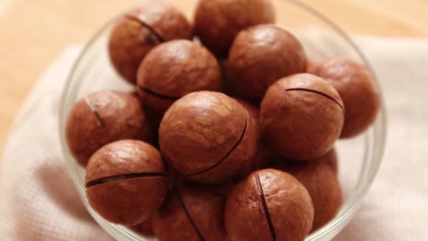 Cerrar cuenco de vidrio con nueces de macadamia orgánica en la mesa sobre fondo de madera . — Vídeos de Stock