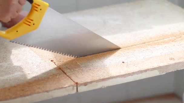 Una mano humana con una sierra corta un aglomerado en una casa . — Vídeos de Stock