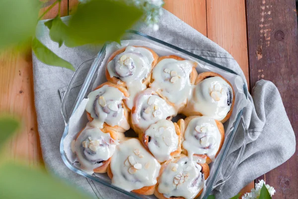 Top view of fresh tasty cinnamon rolls with cream and almonds on a wooden table with white turns of lilac on a sunny day, flat lay — Stock Photo, Image