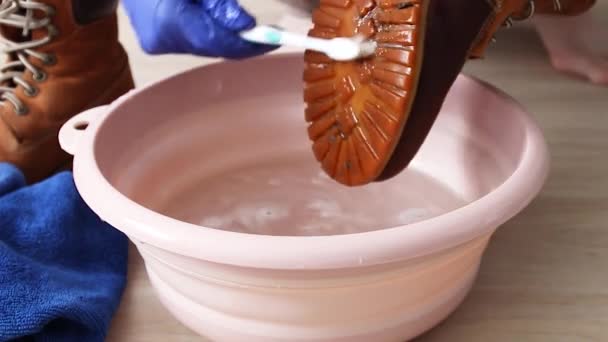 Washing dirty shoes at home. Female hands wash dirty shoes from dirt in a pink plastic basin — Stock Video