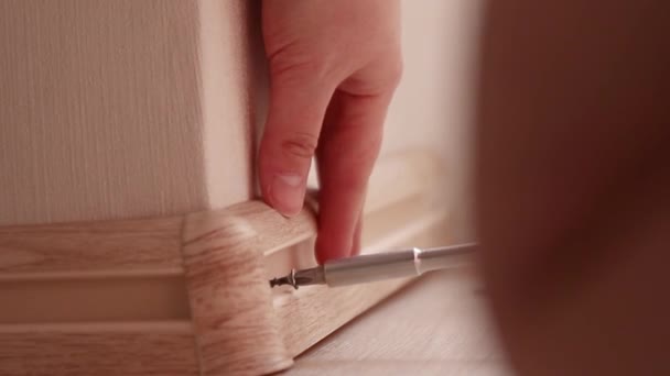 Human hand touches the plastic baseboard with a screwdriver and dowel. Installation and installation of plastic floor plinth — Stock Video