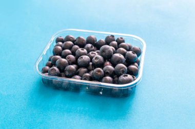 Ormandan taze yabanmersini, mavi arka planda plastik konteynırda.