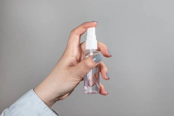 La mano femenina sostiene una botella de plástico con un aerosol desinfectante sobre fondo gris eliminado. Una herramienta para la protección contra el coronavirus, pandemia — Foto de Stock