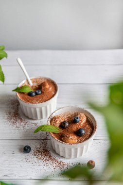 Klasik yaban mersinli tiramisu tatlısı, gri arka planda beyaz kavanozda nane şekeri. Düz konsept