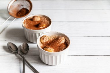 Kakaolu nefis tiramisu tatlısı ve gri arka planda beyaz seramik kavanozlarda savoyardi kurabiyeleri.