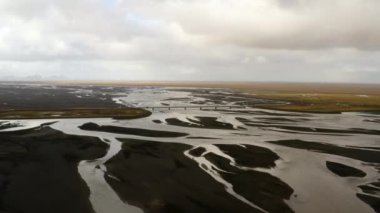 Nehir deltasının hava görüntüsü, Güney İzlanda 'daki siyah volkanik kum, köprüden geçen arabalar, buzul nehirleri, yeşil düz, bulutlu bir gün 4K