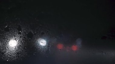 Arka planda yağmurla kaplı bir arabanın ön camından gece bulanık trafik görüntüsü