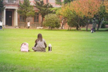 Bulanık, soyut, genç bir kadın. Kamu parkındaki çimlerin üzerinde dinleniyor. Bulanık, soyut bir arka plan.