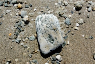 Küçük çakıl taşları ve ıslak kumla çevrili büyük bir çakıl taşı.