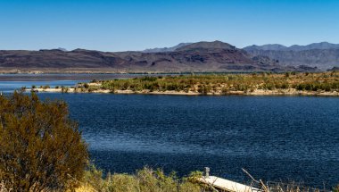 Arizona 'daki Alamo Gölü' nün insansız hava aracı görüntüsü Bill Williams Nehri üzerinde açık mavi gökyüzü ve su, kahverengi tepeler ve mor dağlar ve güzel çöl manzarası.