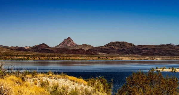Arizona 'daki Alamo Gölü' nün insansız hava aracı görüntüsü Bill Williams Nehri üzerinde açık mavi gökyüzü ve su, kahverengi tepeler ve mor dağlar ve güzel çöl manzarası.