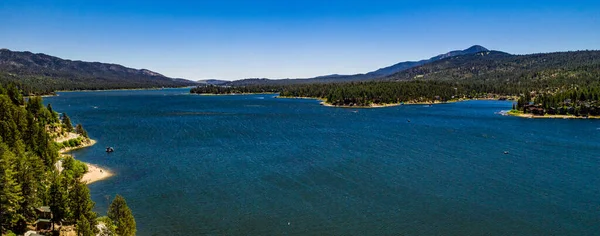 San Bernardino Dağları 'ndaki güzel Büyük Ayı Gölü' nün insansız hava aracı manzarası açık bir yaz gününde mavi su ve gökyüzü, yeşil orman çam ağaçları, mor tepeler ve dağlar
