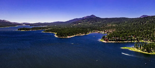 San Bernardino Dağları 'ndaki güzel Büyük Ayı Gölü' nün insansız hava aracı manzarası açık bir yaz gününde mavi su ve gökyüzü, yeşil orman çam ağaçları, mor tepeler ve dağlar