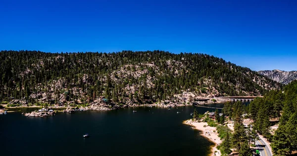 San Bernardino Dağları 'ndaki güzel Büyük Ayı Gölü' nün insansız hava aracı manzarası açık bir yaz gününde mavi su ve gökyüzü, yeşil orman çam ağaçları, mor tepeler ve dağlar