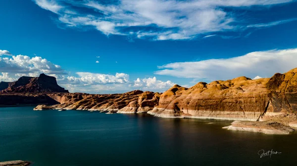 Aerial, panoramic, landscape of beautiful Lake Powell in Utah and Arizona at dusk during monsoon season with red rock hills, blue water and sky, water reflections, white and grey clouds near the San Juan River