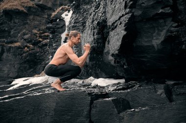 Sportif adam dambıllarla egzersiz yapıyor. Kayalık zeminde çıplak gövdesi olan kaslı modelin fotoğrafı. Fitness ve sağlıklı yaşam tarzı konsepti