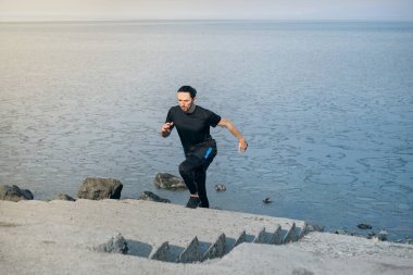 Genç kaslı, sağlıklı yakışıklı aktif adam sabah merdivenlerde koşuyor. Denizde..